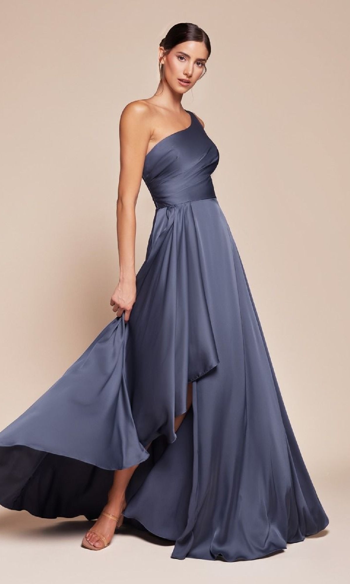 A woman models the One-Shoulder Long A-Line Prom Dress: Ladivine 7450 in slate blue, featuring a flowy asymmetrical hem, standing against a beige background.
